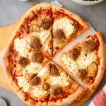 Overhead view of a meatballs and ricotta pizza on a grey background.