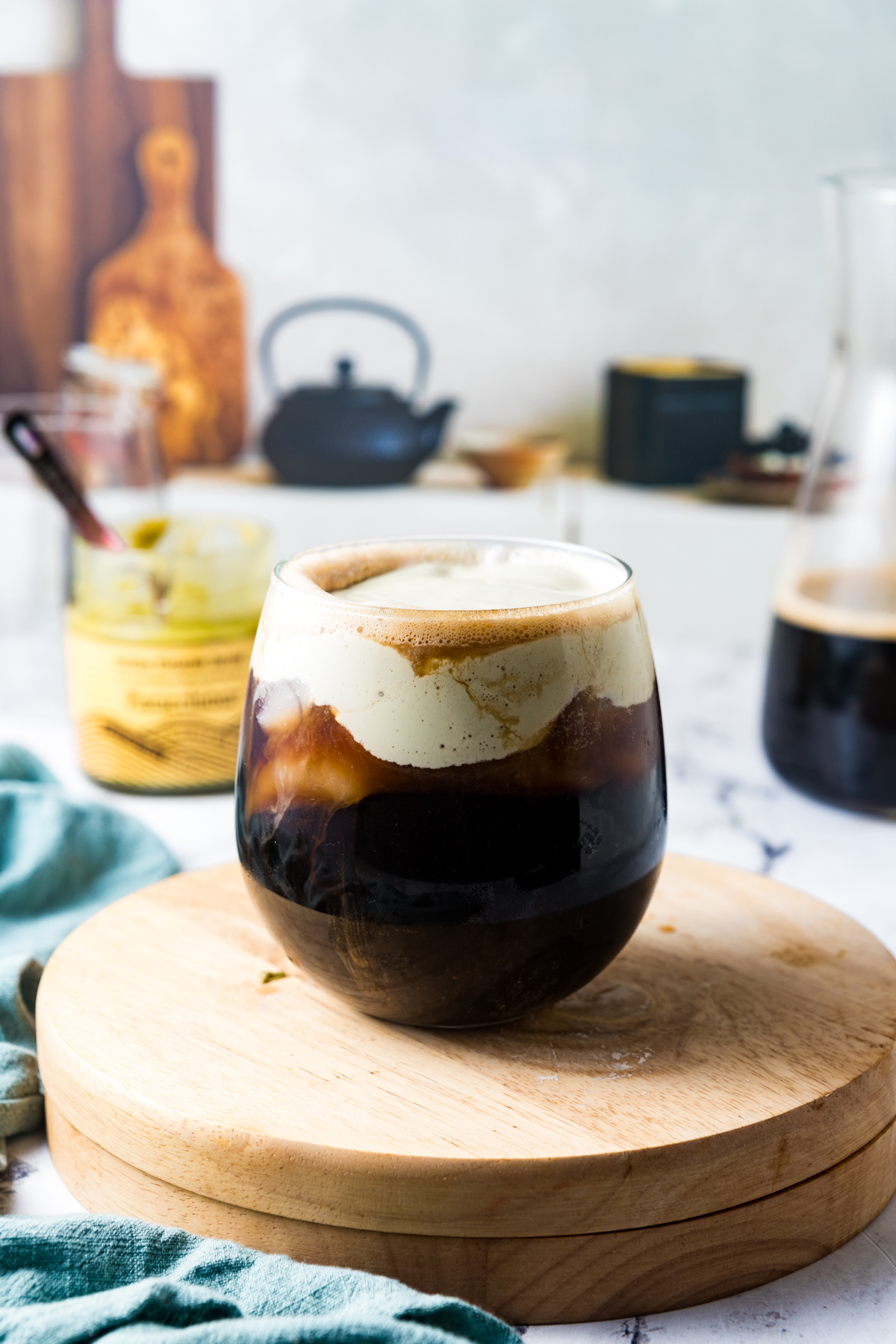 A glass of iced coffee topped with pistachio cold foam on a kitchen counter. 