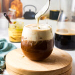 Spooning homemade pistachio whipped cream onto a cold brew coffee.
