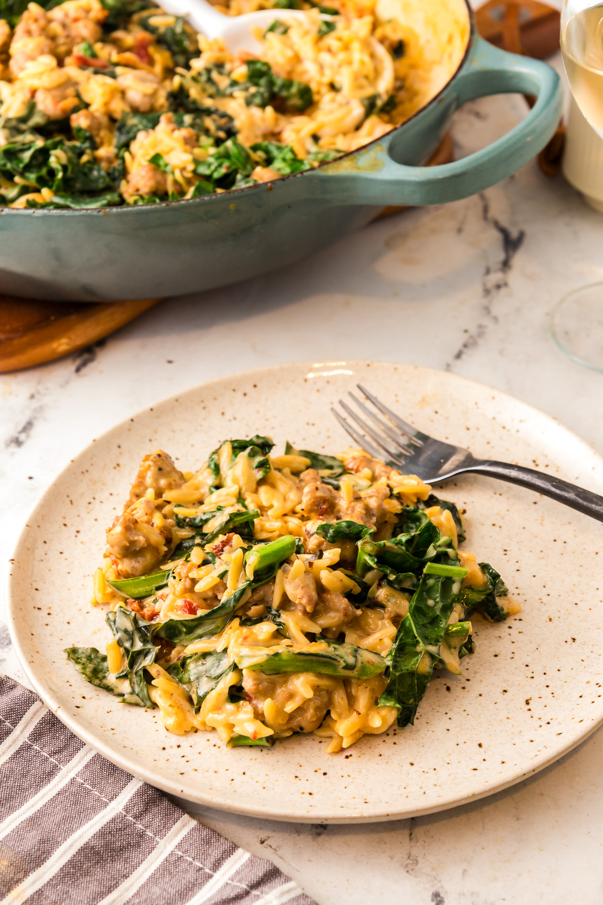 A plate of creamy orzo with sausage and kale in front of a window. 