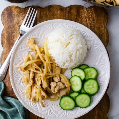 A plate of Cambodian style ginger chicken stir fry with rice and cucumber.