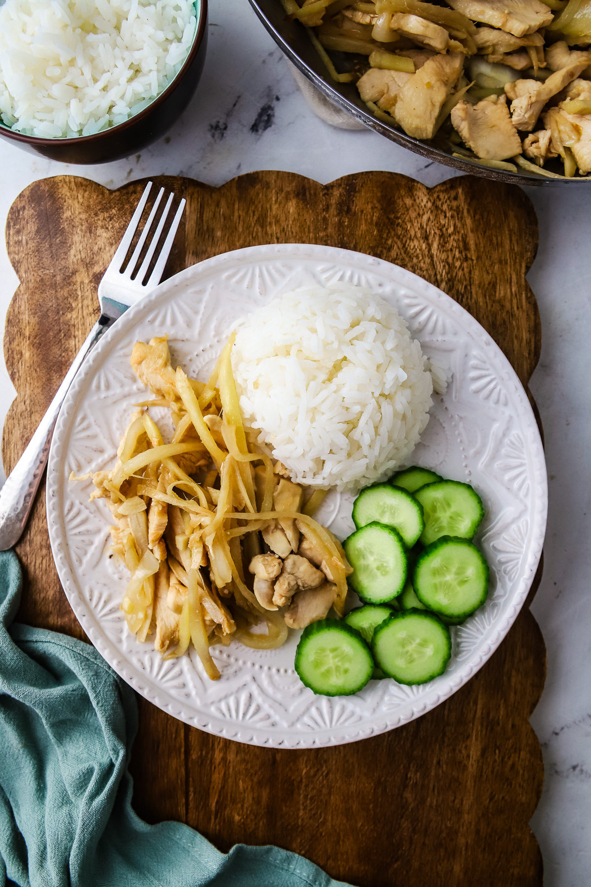A plate of Cambodian style ginger chicken stir fry with rice and cucumber.