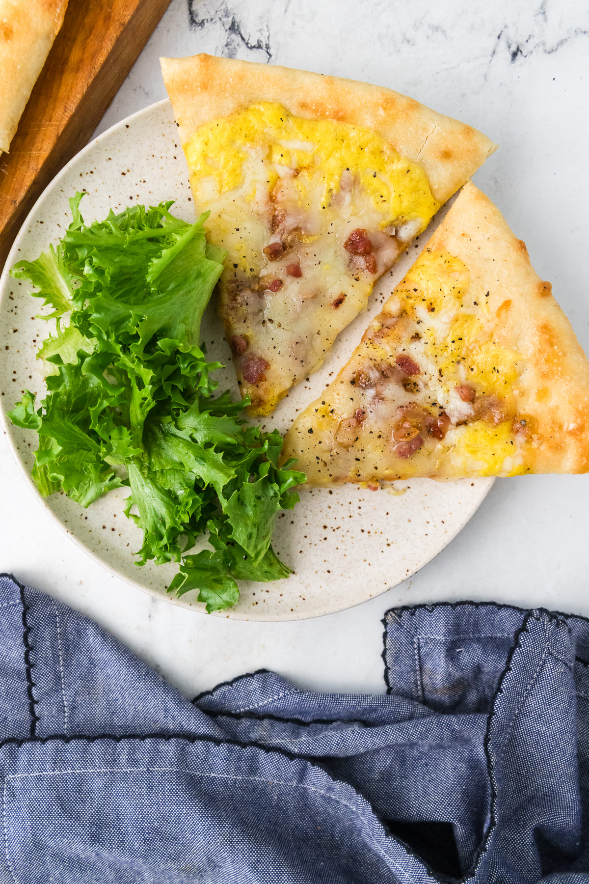 Two slices of carbonara pizza on a plate with salad.
